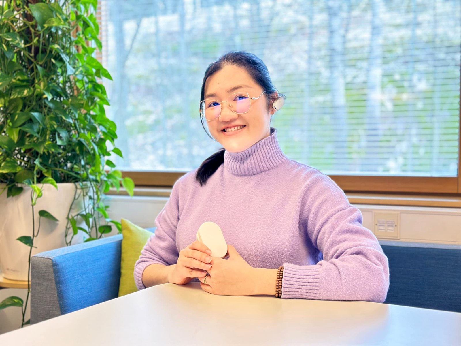 Smiling woman wearing EVANES on her left ear, holding the open charging case